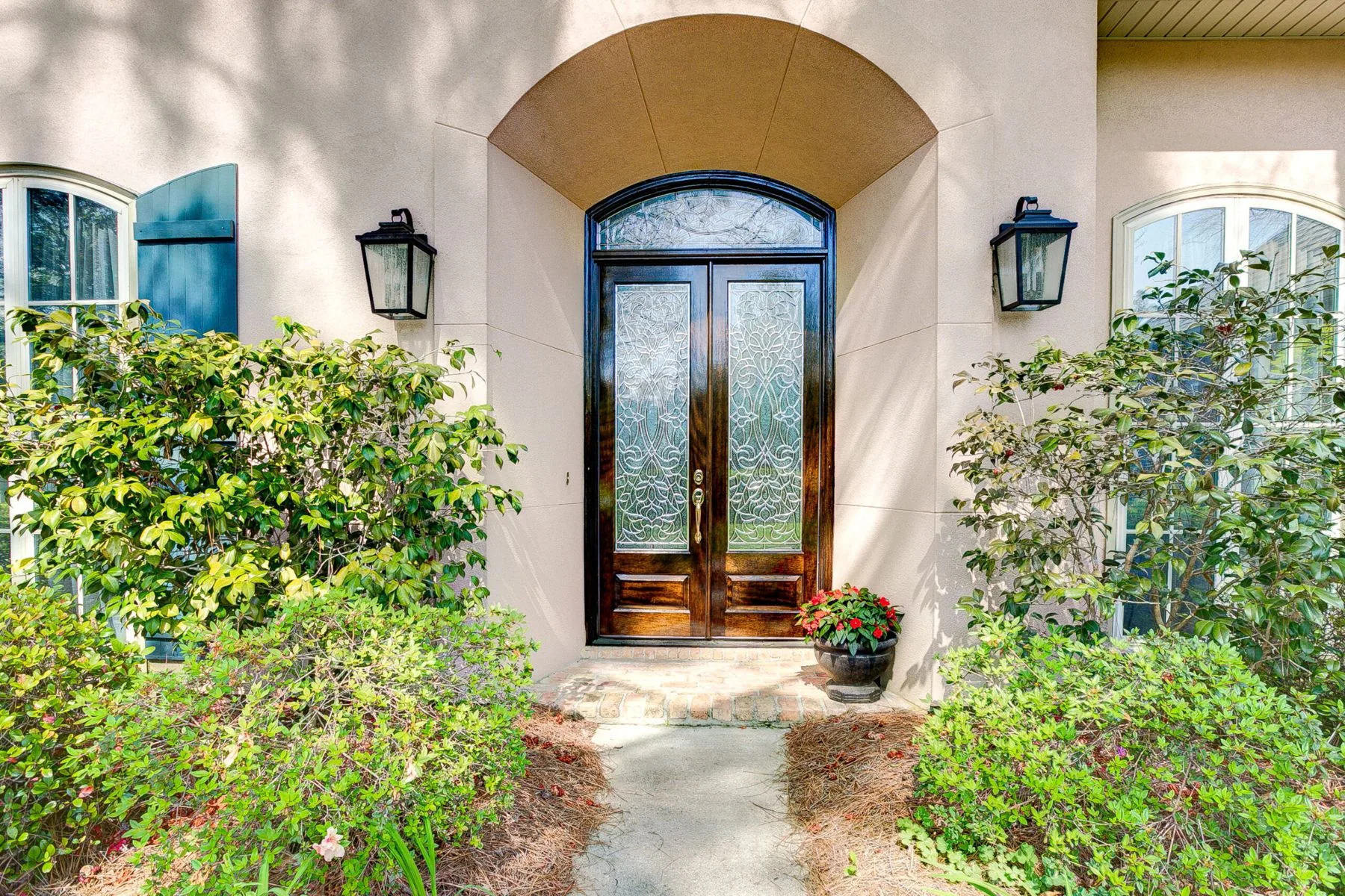 Arched mahogany double doors with leaded glass and transom on a stucco home